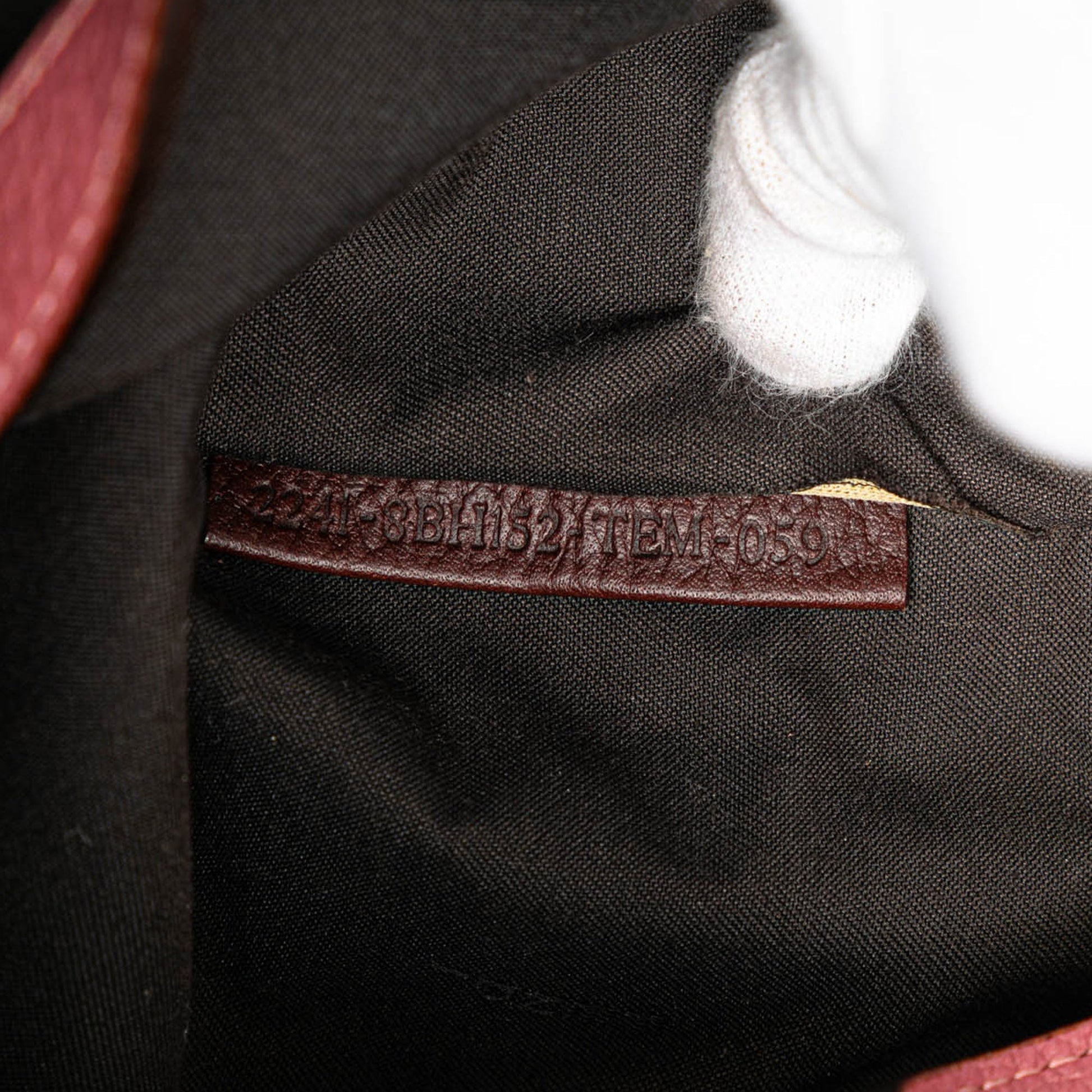 Close-up of Fendi logo charm on burgundy leather strap with gold-tone hardware